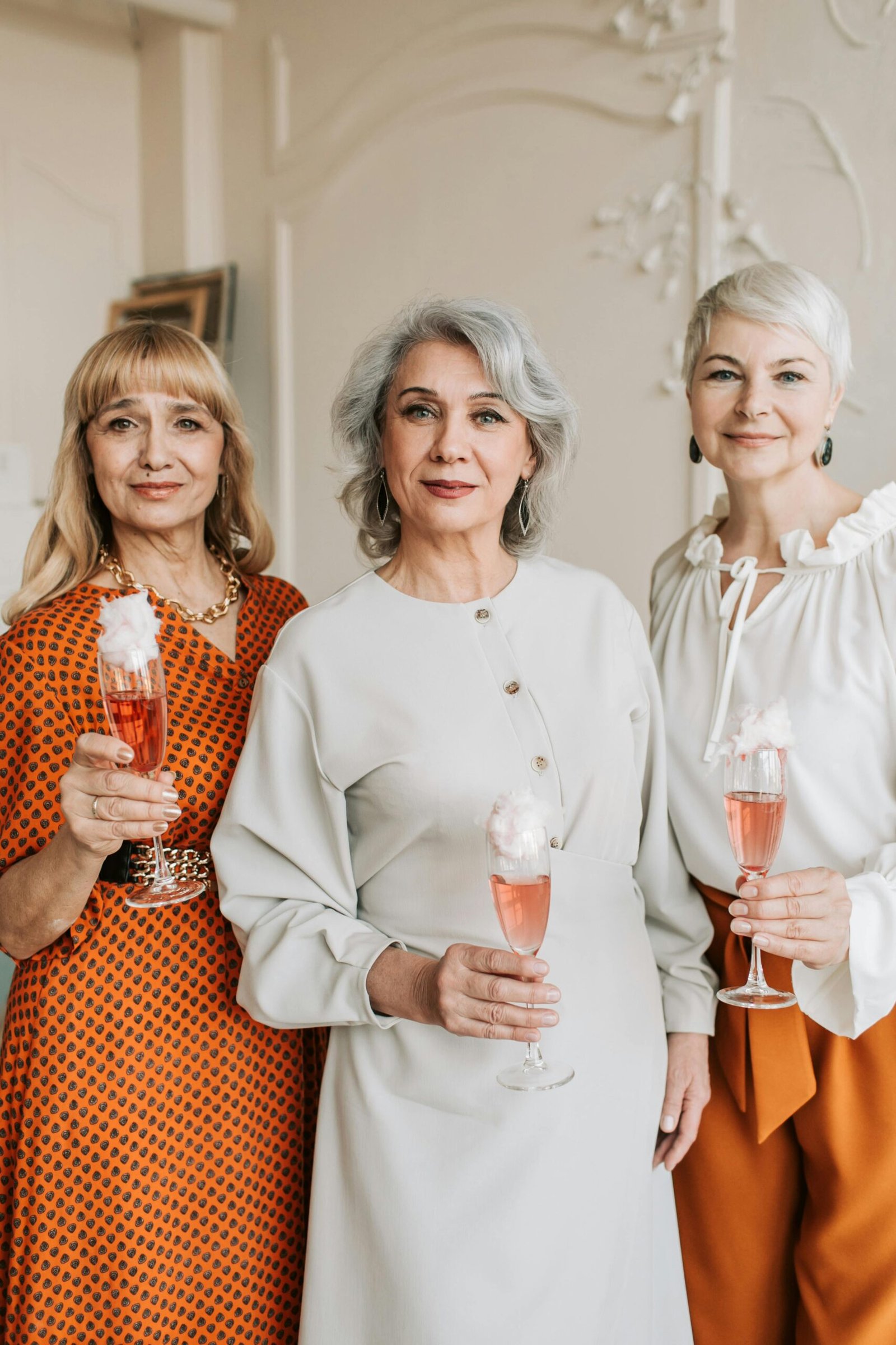 Three senior women holding champagne glasses, celebrating indoors with smiles.